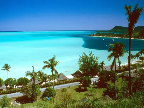 White‑sand Matira beach meeting calm lagoon, with a hotel silhouette on the far right horizon