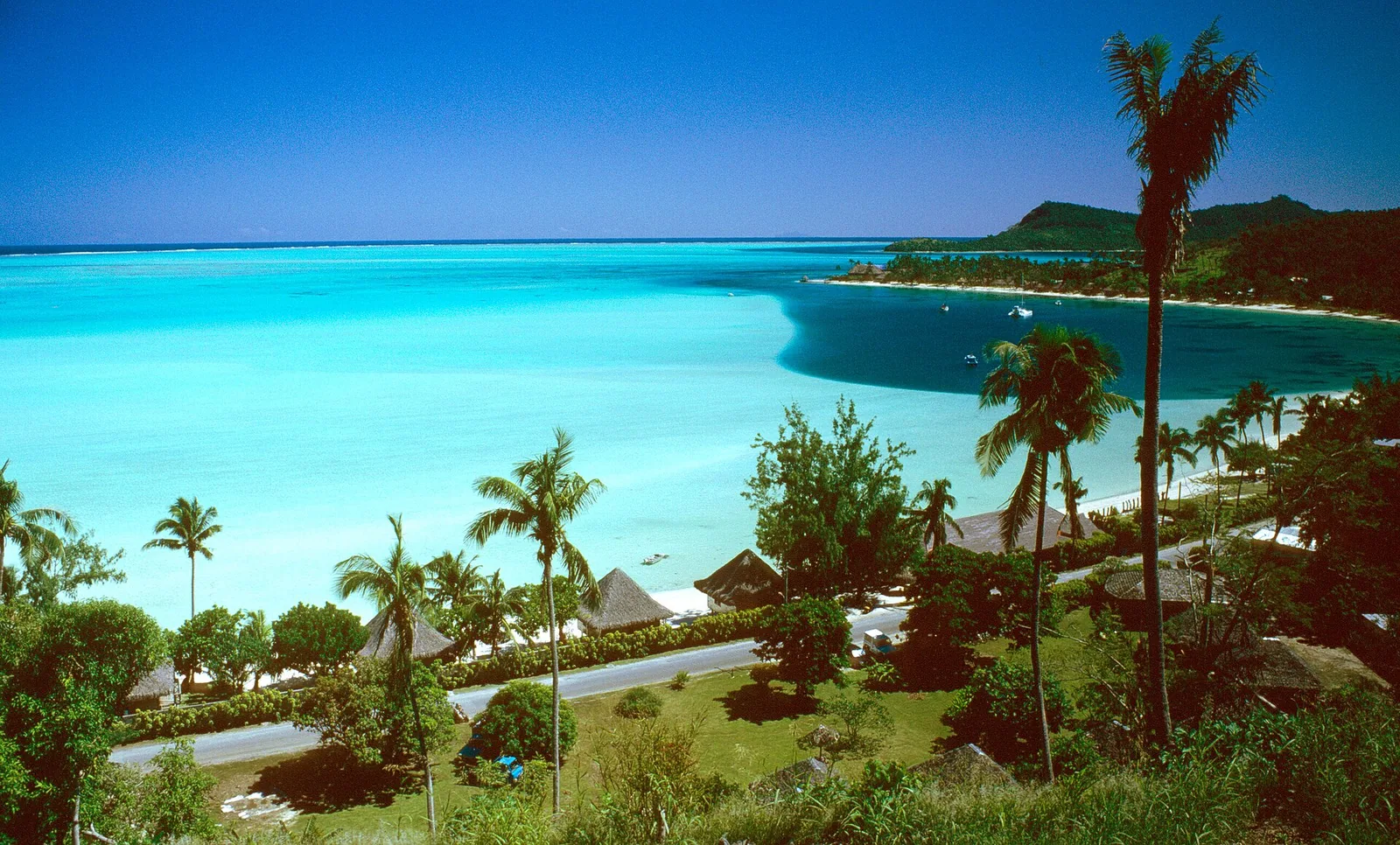 White-sand Matira beach meeting calm lagoon, with a hotel silhouette on the far right horizon