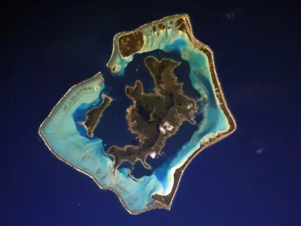 Satellite‑style view of Bora Bora’s reef and lagoon from space, showing vivid blue waters