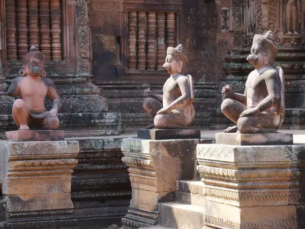 Carved guardian statues in front of the red sandstone shrines of Banteay Srei