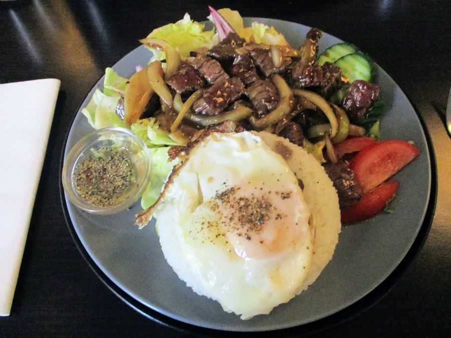 A plate of beef lok lak with a fried egg and salad