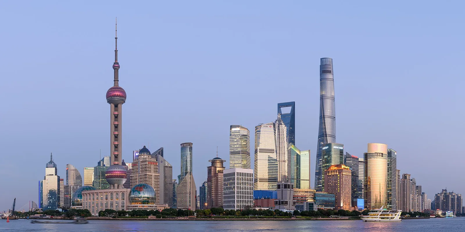 Panoramic view of Shanghai's Pudong skyline, showing skyscrapers, Huangpu River and distant hills.