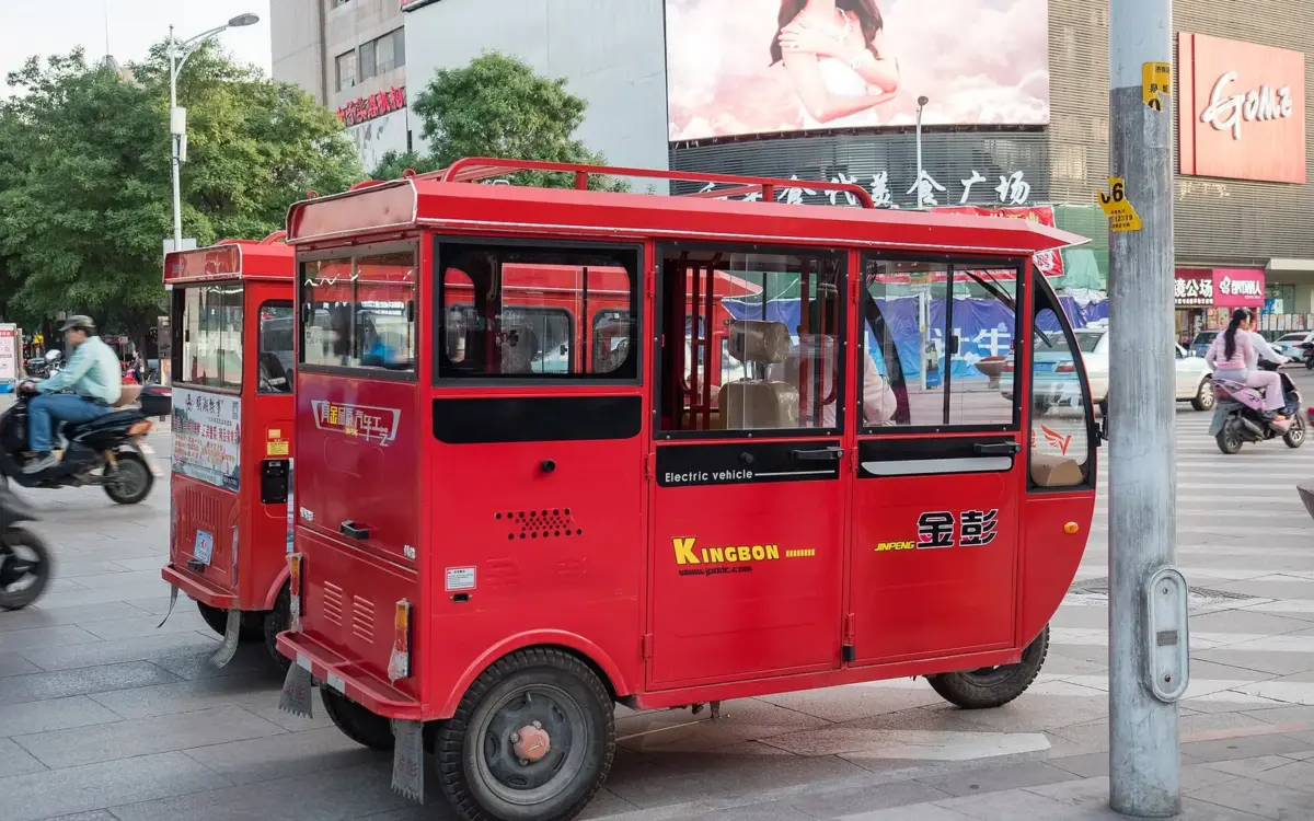 Small yellow taxi parked on a street in Jinan, with city buildings and traffic signs nearby.
