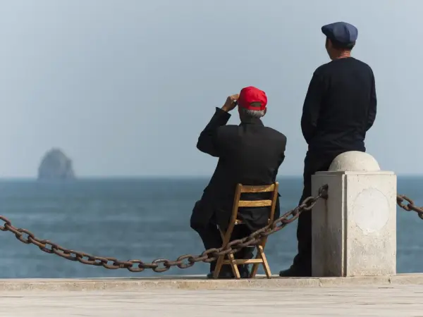 Two elderly Chinese men standing on the beach at Xinghai Bay, Dalian, watching the sea.