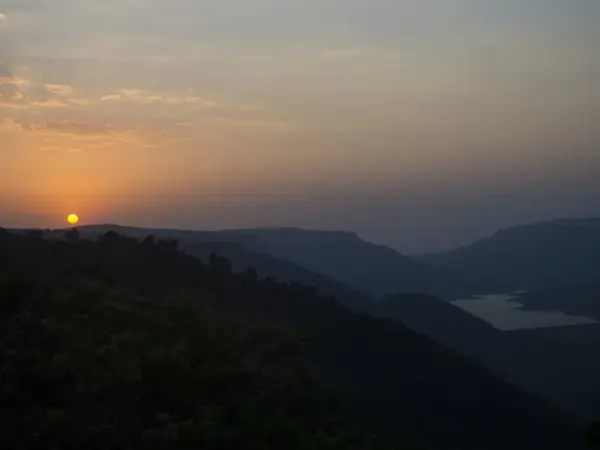 Sunset over Dhom Lake, orange sky reflected on calm water near Mahabaleshwar