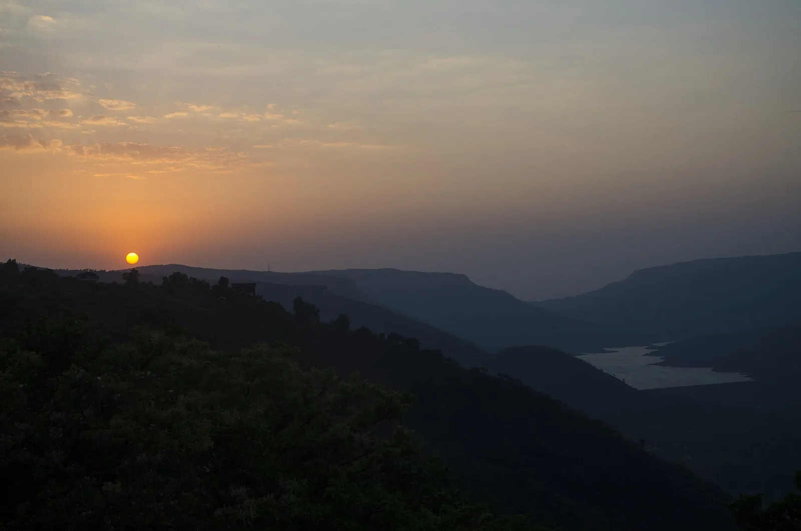 Sunset over Dhom Lake, orange sky reflected on calm water near Mahabaleshwar